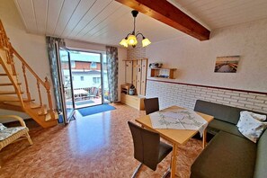 A spacious living area with a wooden staircase, a dining table with chairs, a sofa, and a large window with a view of the outside. - Groth holiday apartments (Heringsdorf (Seebad))