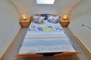 A small, cozy bedroom with a bed, floral pillows, bedside lamps, and a skylight. - Groth holiday apartments (Heringsdorf (Seebad))