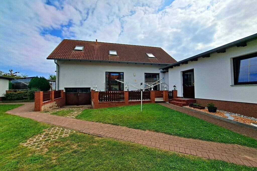 A single-story house with a tiled roof, a fenced yard, and a brick pathway leading to the entrance.