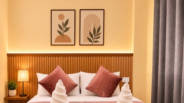 Una habitación de hotel con una cama, dos almohadas, una lámpara de noche y una pared con dos cuadros enmarcados.