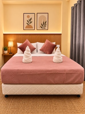 A hotel room with a bed, two pillows, a bedside lamp, and a wall with two framed pictures.