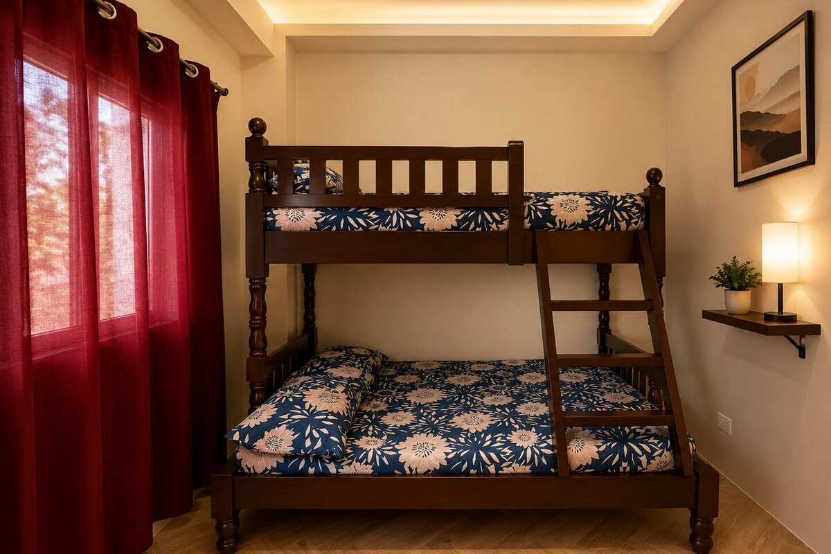 A bunk bed with floral bedding, a bedside lamp, and a red curtain.