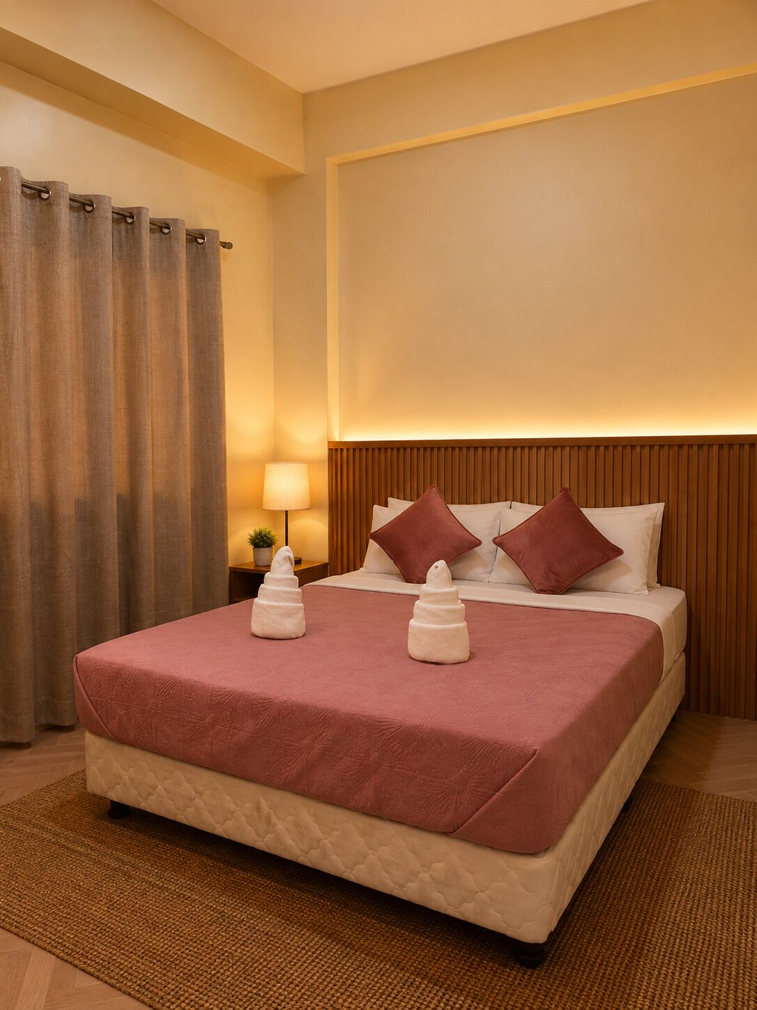 A hotel room with a bed, pillows, a nightstand, a lamp, and a curtain.