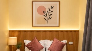 Habitación de hotel con cama, mesita de noche con lámpara, un cuadro en la pared y una ventana con cortinas.