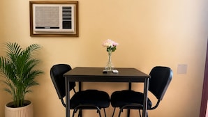 Un comedor con una mesa, cuatro sillas, una planta en maceta, un florero con flores y un equipo de aire acondicionado instalado en la pared.