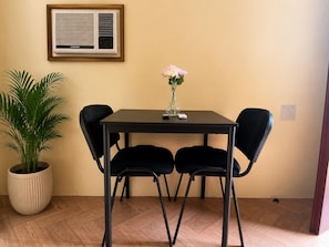 A dining area with a table, four chairs, a potted plant, a vase with flowers, and a wall-mounted air conditioning unit. - RV3 Transient House (Angeles)