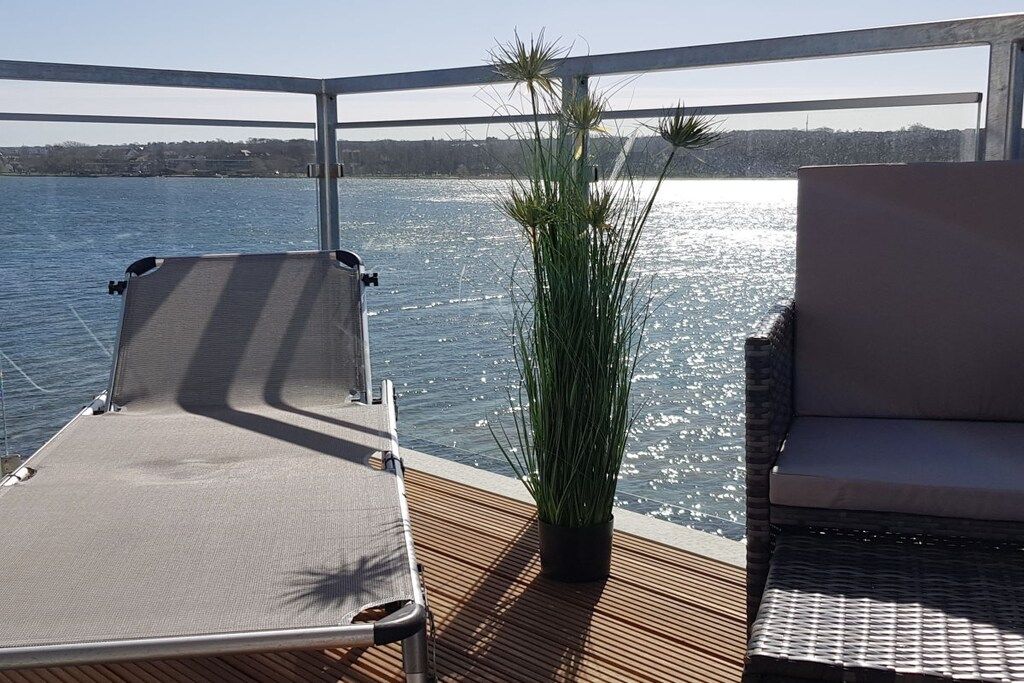 A deck with a lounge chair and a potted plant, overlooking a body of water.