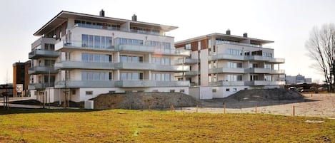 Un edificio residencial de varios pisos con balcones, techo plano y un sitio de construcción en primer plano.