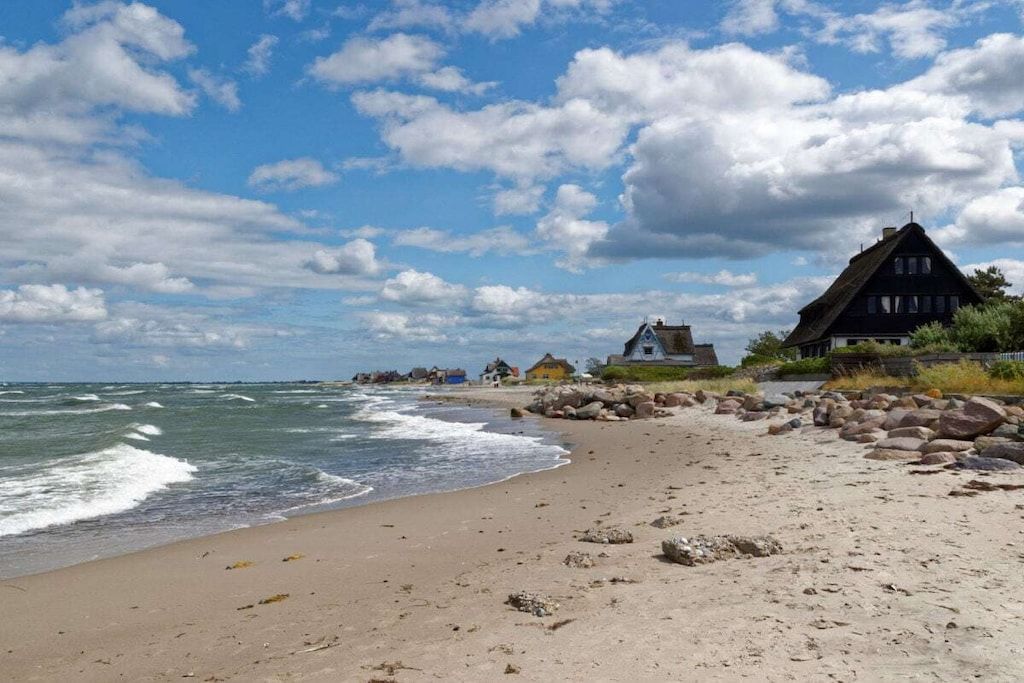 Uma praia com uma casa de telhado de palha, margem arenosa e céu claro.