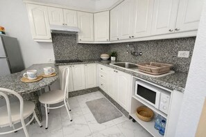 Cuina amb armaris blancs, encimeres de granit, un rentaplat i microones, i zona de menjador amb cadires i taula.