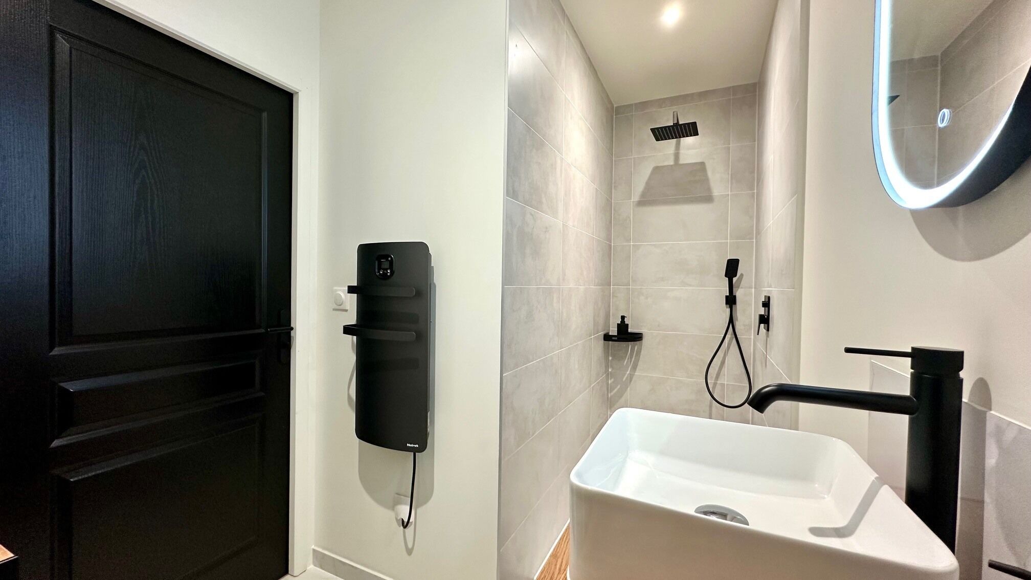 Ein Badezimmer mit einem weißen Waschbecken, einem schwarzen Handtuchspender und einer Duschkabine mit einer Handbrause.