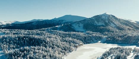 A snow-covered landscape with a mountain, a lake, and buildings.