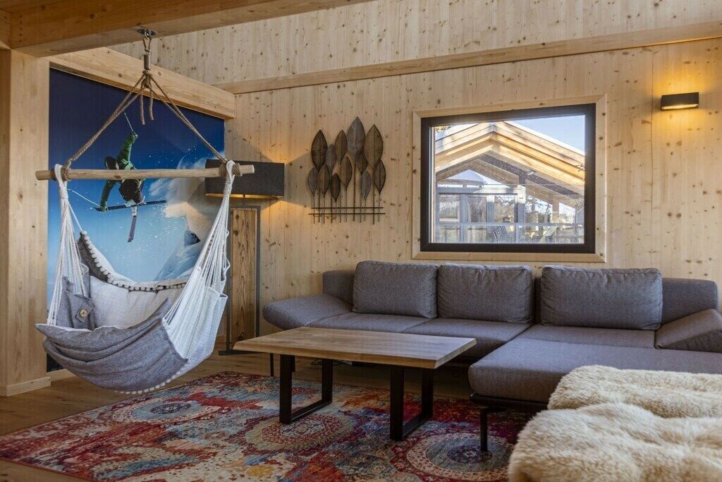 Ein Zimmer mit einer Hängematte, einem Sofa, einem gemusterten Teppich und einem Fenster mit Blick.