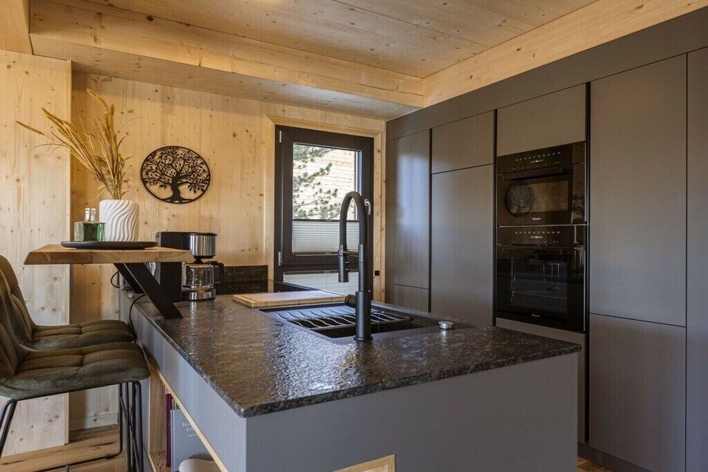 A modern kitchen with a granite countertop, stainless steel appliances, and a wooden ceiling.