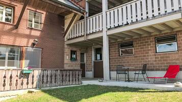 Een gebouw met twee verdiepingen, een bakstenen gevel, een balkon met witte relingen en een klein terras met stoelen en een tafel.
