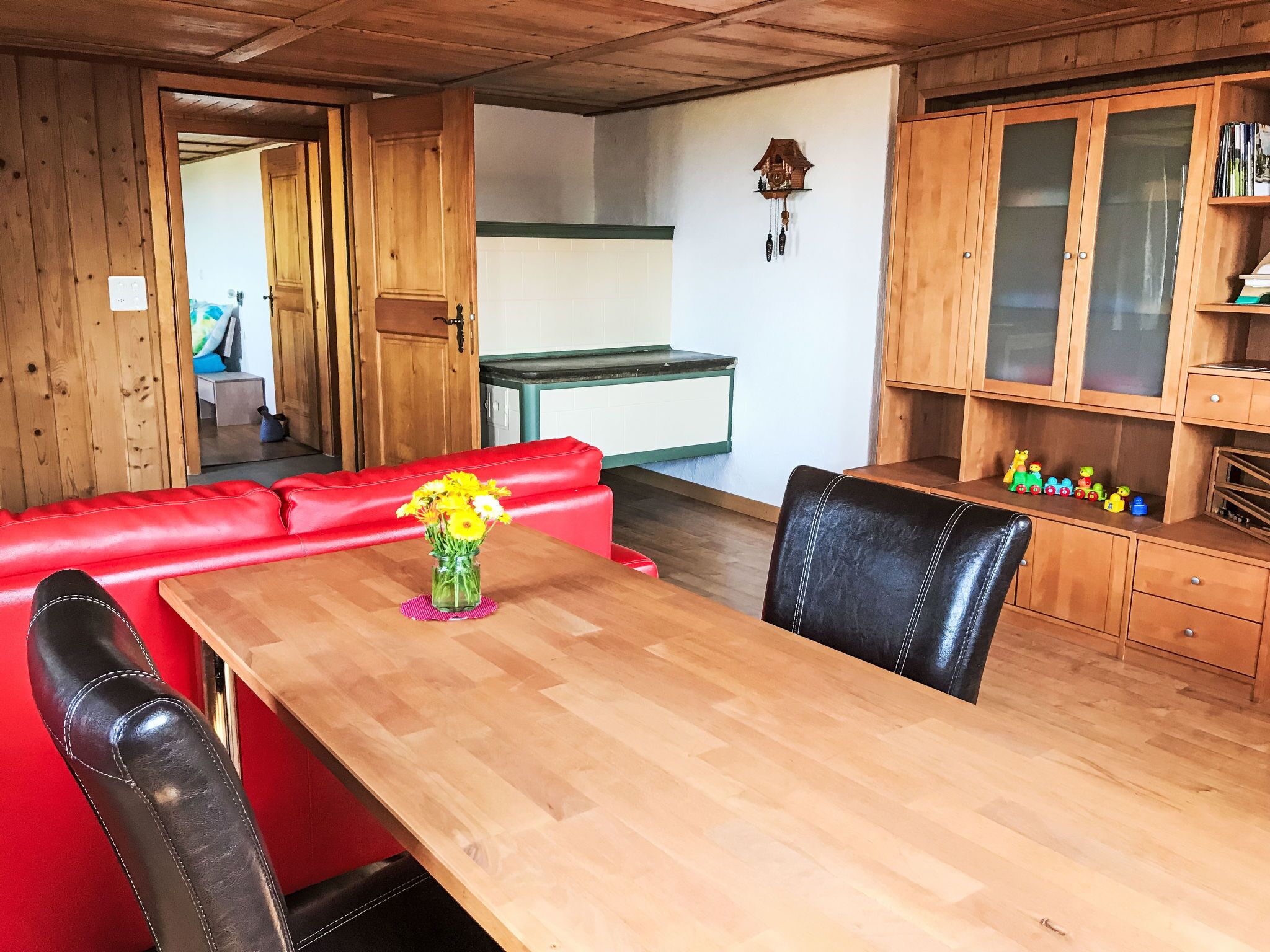 A wooden dining table with a vase of flowers, a red sofa, and black leather chairs.