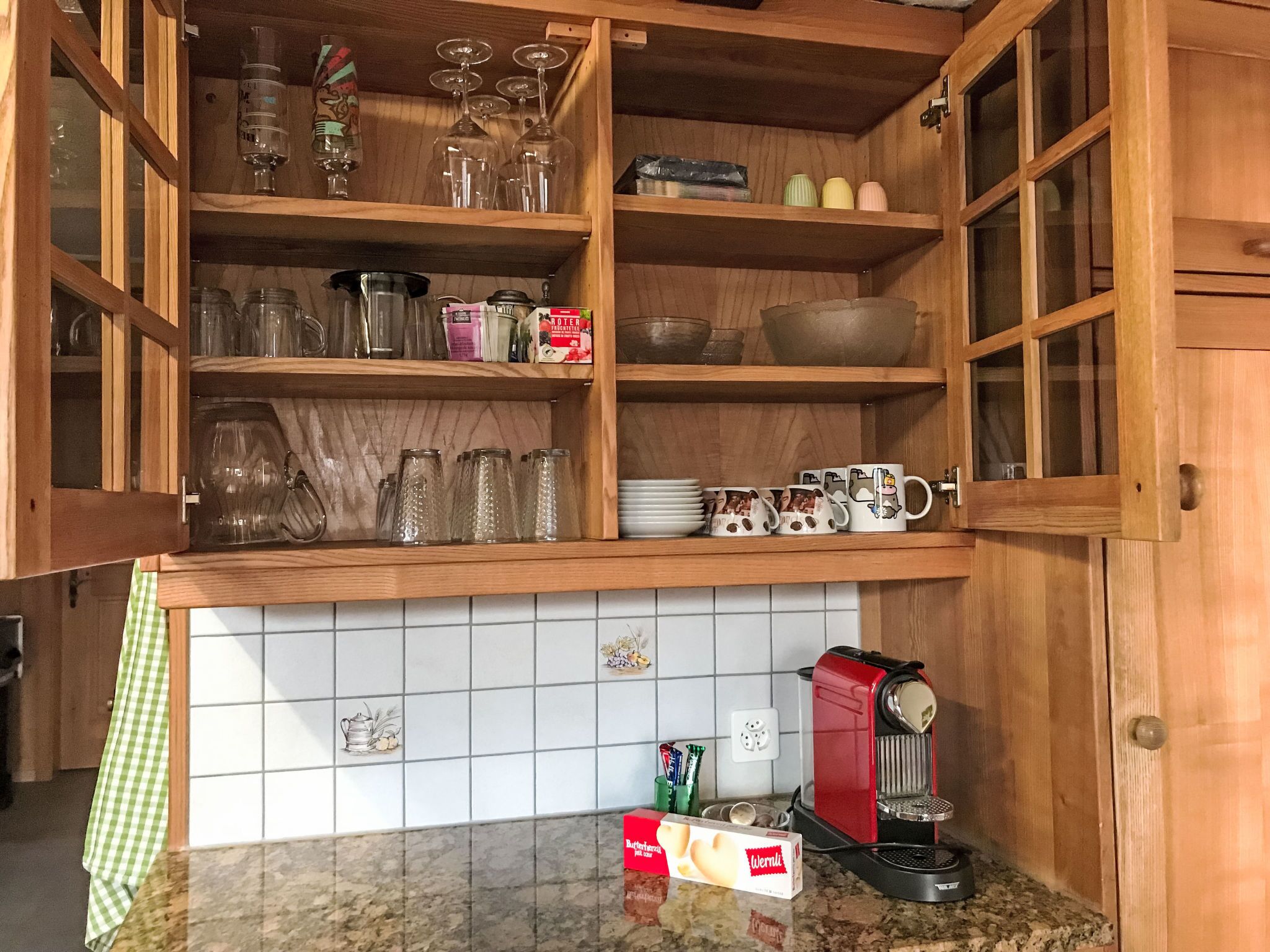 Een keuken met open houten kastjes, een koffiezetapparaat en divers keukengerei.
