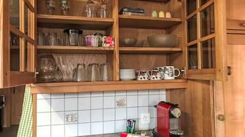 Een keuken met open houten kastjes, een koffiezetapparaat en divers keukengerei.