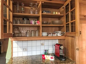 Una cocina con armarios de madera abiertos, una cafetera y diferentes utensilios de cocina.