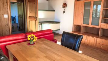 Et træbord med en vase blomster, en rød lædersofa og en sort læderstol i et rum med trævægge og -skabe.