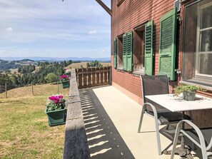 Una terraza con mesa y sillas, vistas al campo y un edificio con contraventanas verdes.