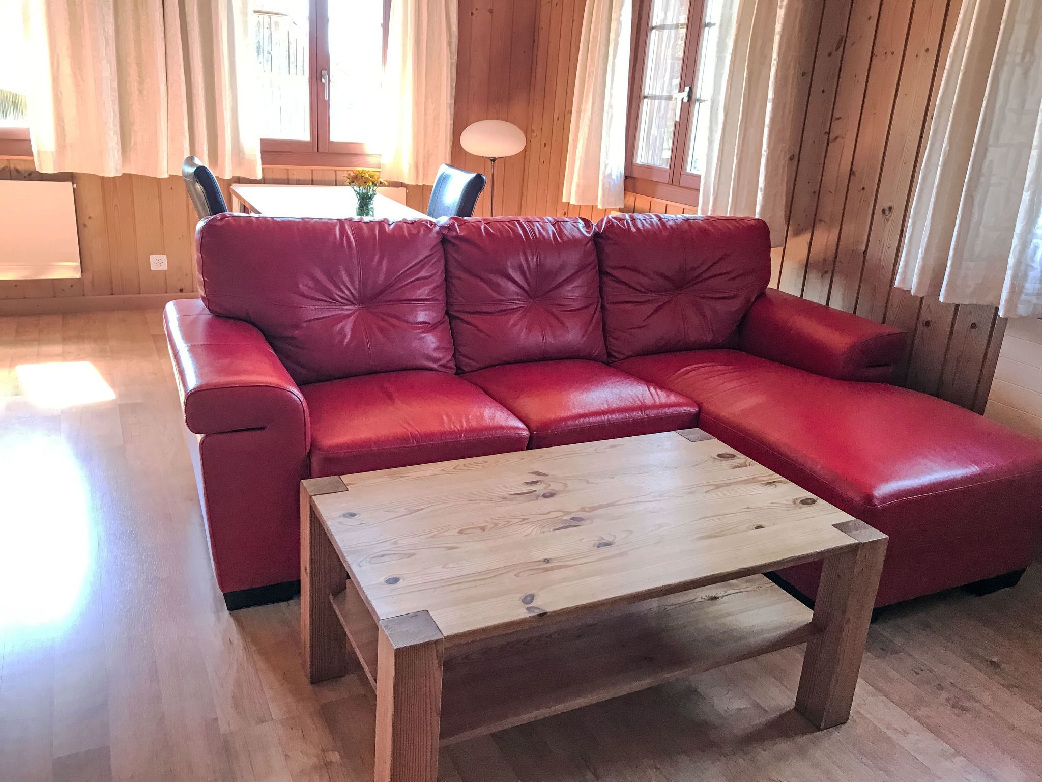 Un sofá de cuero rojo con una mesa de centro de madera en una habitación con paredes de madera y un ventanal.