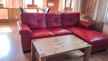 Een rode leren bank met een houten salontafel in een kamer met houten wanden en een raam.