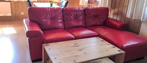 A red leather sofa with a wooden coffee table in a room with wooden walls and a window.