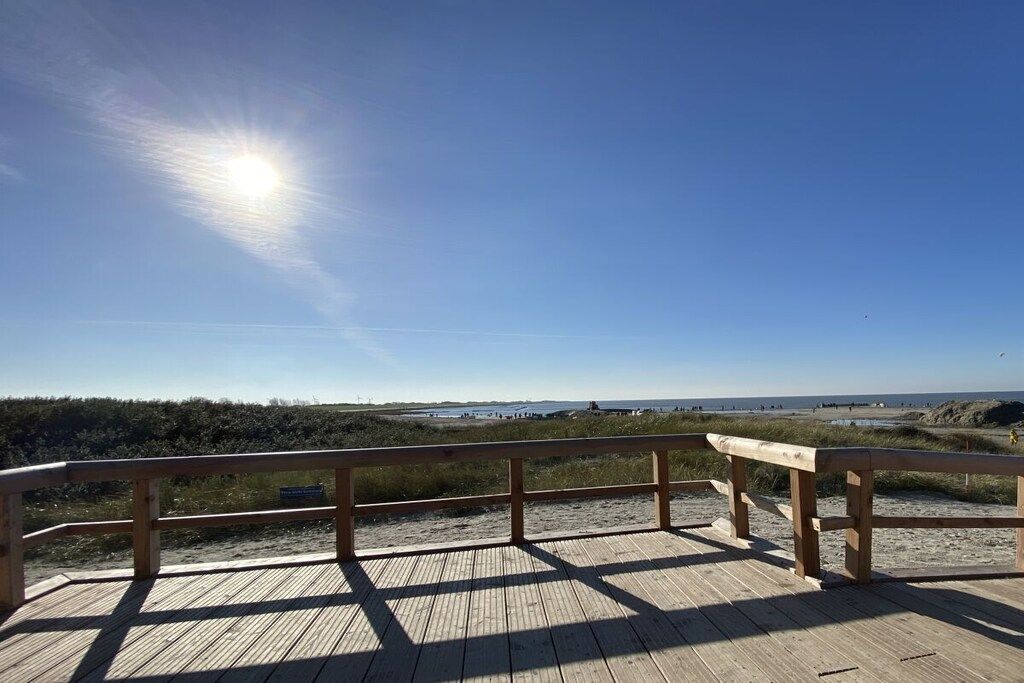 A wooden deck with a railing overlooking a beach.