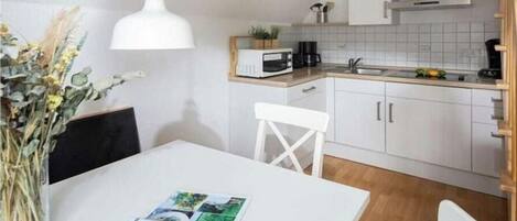 Una cocina moderna con armarios blancos, una mesa de comedor blanca y una lámpara colgante.