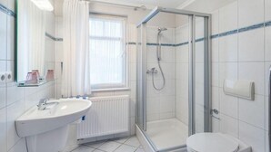 A modern bathroom with a glass-enclosed shower, a white sink, and a toilet. - Marienstraße 4a Apartment 4 (Norderney)