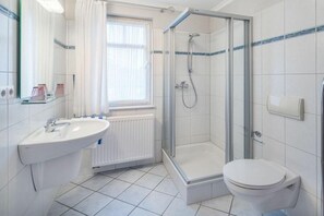 Ett modernt badrum med en dusch som är avskärmad med glasväggar, ett vitt handfat och en toalett.