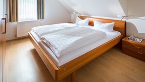 A single bed with a wooden frame, white bedding, and a nightstand with a lamp. - Marienstraße 4a Apartment 4 (Norderney)