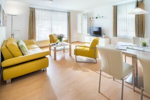 En moderne stue med et gult sofasæt, et sofabord og et spiseområde med stole.