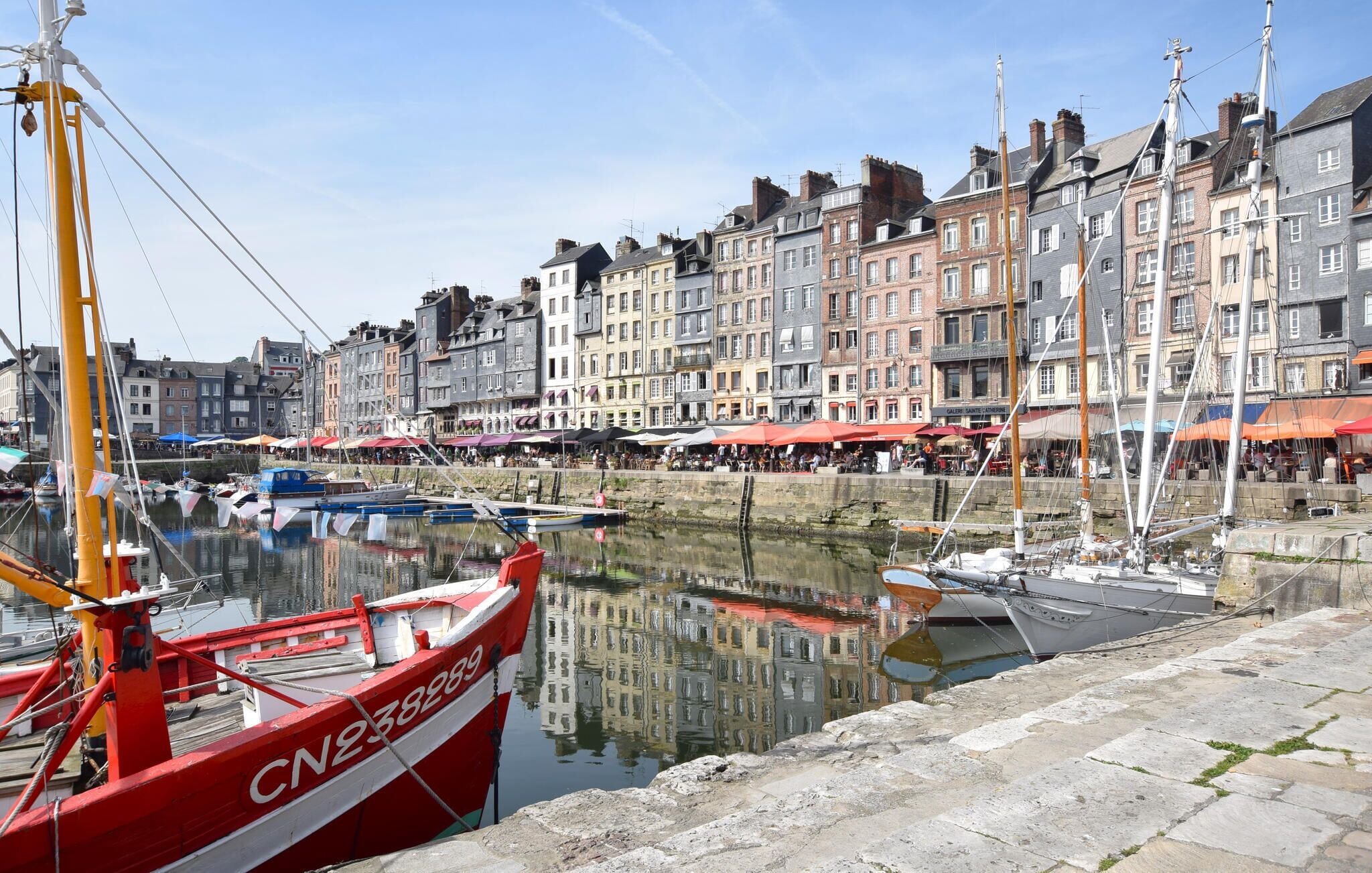 A waterfront with boats docked, a stone quay, and historic buildings with shops.