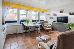 A compact living space with a dining area, a television, and a window with curtains. - Holiday apartment in Norderney with Wi-Fi (Norderney)