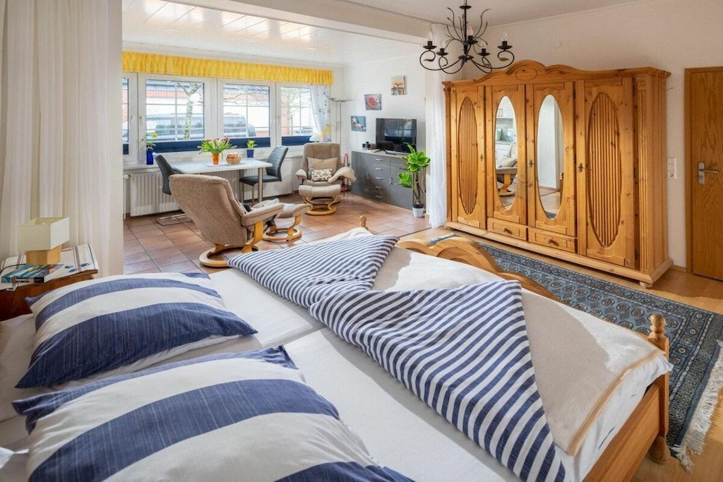 A bedroom with a bed, a wooden wardrobe, and a desk area with a chair and a television.