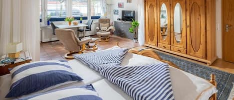 A bedroom with a bed, a wooden wardrobe, and a desk area with a chair and a television.