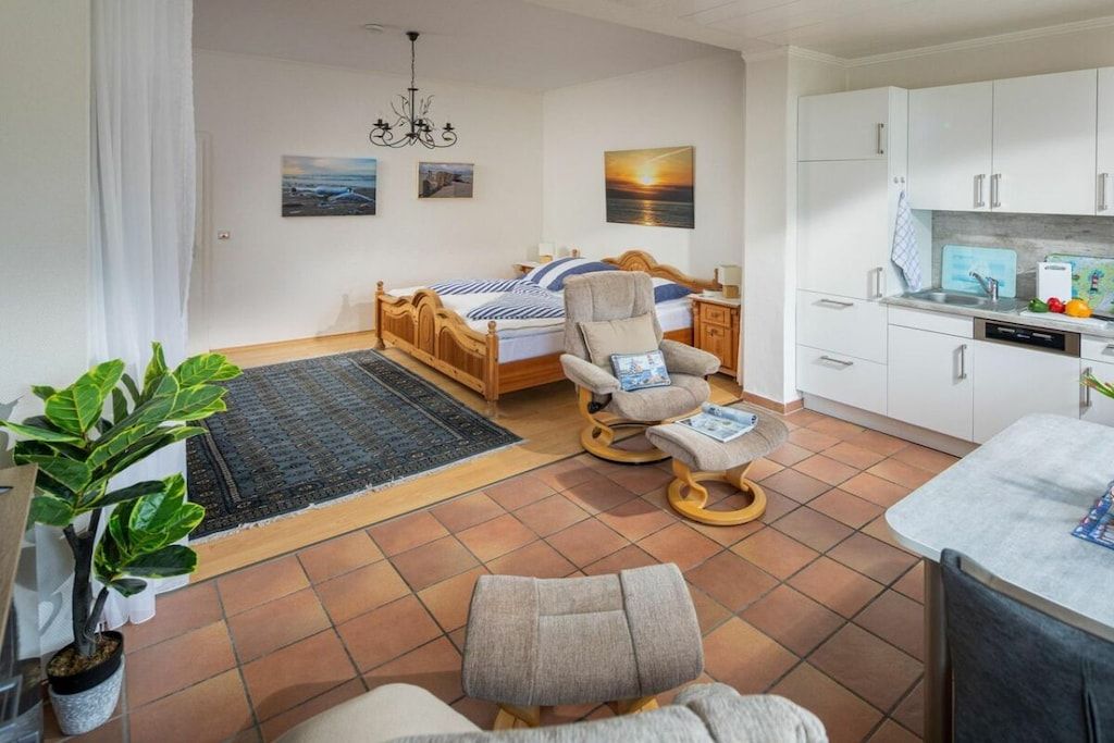 A bedroom with a bed, a chair, a desk, a dining area, and a kitchen.
