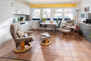 A modern kitchen with white cabinets, a dining table with chairs, and a yellow window valance. - Holiday apartment in Norderney with Wi-Fi (Norderney)