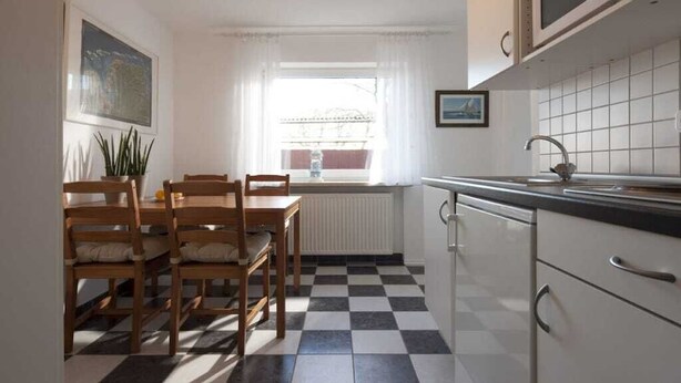 A kitchen with a checkered floor, a dining table with chairs, a window with curtains, and a microwave above the counter. - Holiday apartment with 1 bedroom (Norderney)