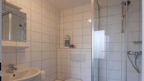 A bathroom with a white sink, toilet, and a glass-enclosed shower area. - Holiday apartment with 1 bedroom (Norderney)