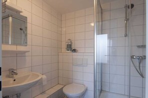 Ett badrum med ett vitt handfat, en toalett och en duschhörna med glasväggar.
