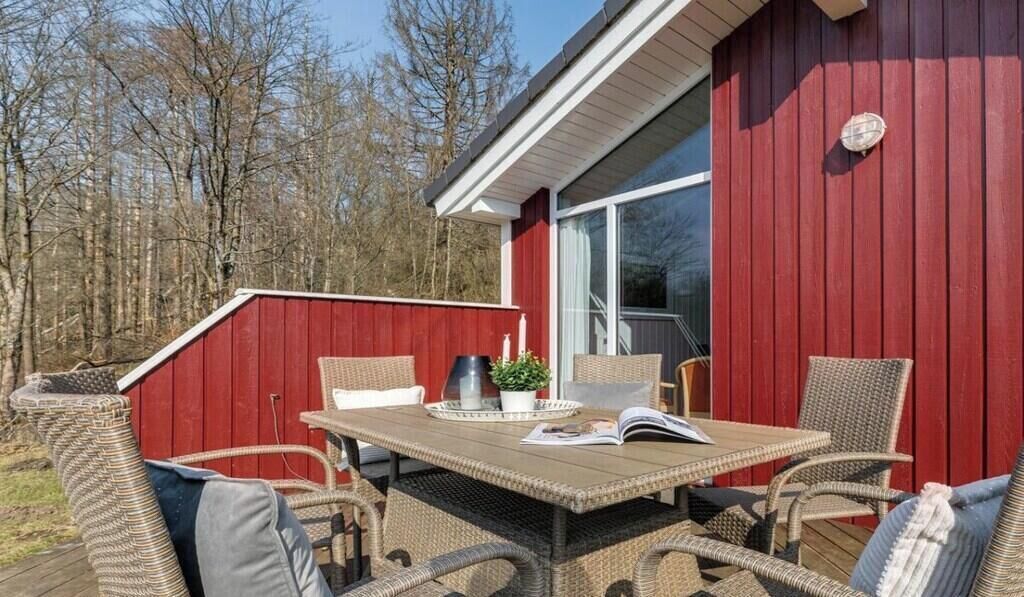 Une terrasse extérieure avec des meubles en osier, une table et, en arrière-plan, un bâtiment rouge.