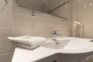 Un baño con lavamanos blanco, una toalla, un espejo y un secador de pelo.