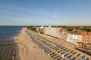 Un hotel frente a la playa con una hilera de sombrillas, una playa arenosa y edificios al fondo.