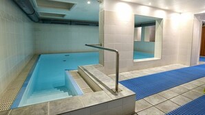 En swimmingpool med en glasvägg som avgränsning, trappsteg som leder ner i poolen och en blå matta på botten.