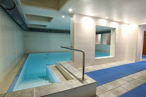 Una piscina con barrera de vidrio, escalones para entrar y un tapete azul en el suelo.