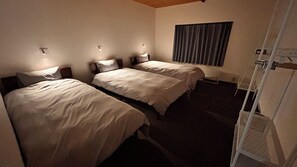 Ein Hotelzimmer mit zwei Einzelbetten, einem Fenster mit Vorhängen, einem Heizkörper und einer Tür mit Metallgriff.