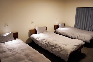 Ein Hotelzimmer mit drei Einzelbetten, einem Holzkopfende, einem Nachttisch und einem blauen Vorhang.